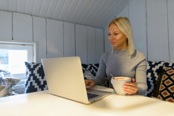 Fototapeta premium Young beautiful blonde woman drinking coffee while using laptop at home