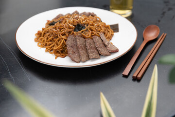 Korean black bean sauce, Jajjangmyeon noodles with sliced beef on top with wooden spoon and chopstick.