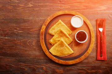 Homemade hot delicious pancakes with sour cream and jam on a wooden plate, top view.