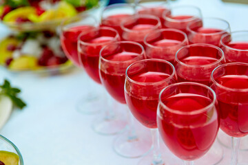 A row of glasses with red drinks, juice, champagne or wine at a party. Catering. Glassware on the table with a white tablecloth. Festive buffet for the holiday.