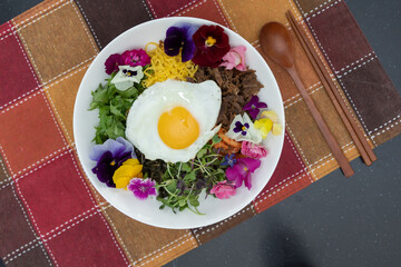 Colorful edible flowers with fried egg food on a bowl with wooden eating utensils