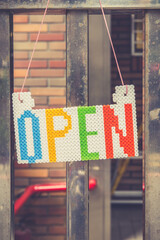 An "Open" sign hanging on a metal door. Toned image.