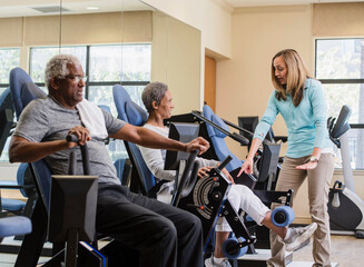  senior couple exercising with trainer in gym