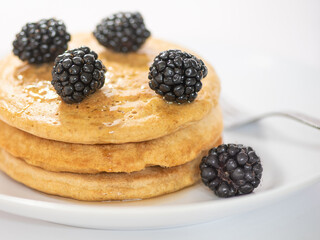 Three pancakes with blackberry on white plate against white background with a fork, selective focus and cropped, with copy-space