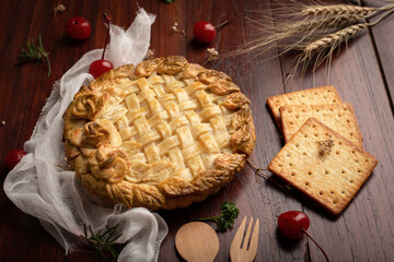 Apple pie with red cherry on wooden table.