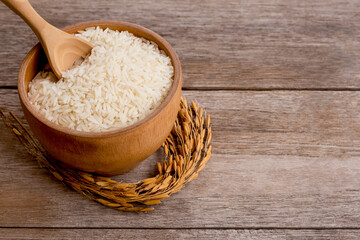 White rice, natural long rice grains (Thai jasmine rice) in wooden bowl and paddy rice isolated on old rustic wood table background.
