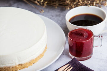 Ice box cheese cake with strawberry jam and a cup of coffee on the table.