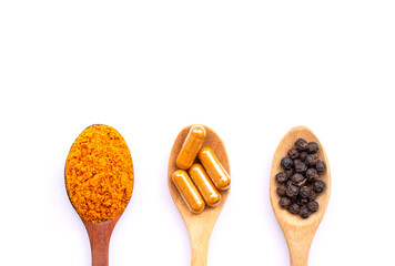Tumeric powder, Curcumin capsule and black pepper corn in wooden spoon  isolated on white background.  Natural herbal medical plant concept. Top view. Flat lay.