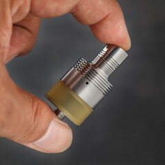high end titanium genesis atomizer with amber ultem tank section in hand on dark texture...
