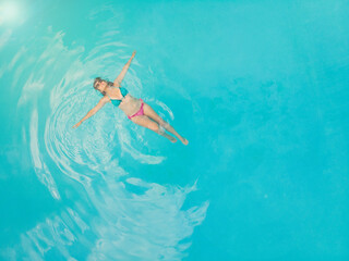 Aerial view of a relaxed young woman in the transparent turquoise sea. Top view of slim woman relaxing in hotel pool.