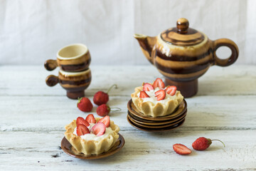 Dessert tartlets with butter cream and fresh strawberries on a white wooden background. Ceramic tableware for saina or coffee ceremony. Horizontal orientation