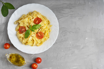 Top view of cooked italian fettucine pasta in white plate decorated with basil leaves on gray concrete background surrounded by olive oil gravy boat, cherries and spinach. Image with copy space