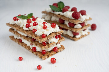 Closeup view of healthy sandwiches made of crisp bread, ricotta and red berries decorated with mint leaves on white wooden background ready for eating at kitchen. Image with selective focus