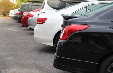 Closeup of rear, back side of black car with  other cars parking in outdoor parking area.