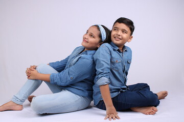 Two cute Indian kids in twinning dress concept sitting together on white background.