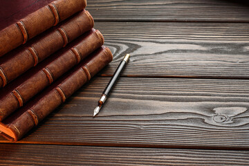 Stack of old leather-bound books and fountain pen on wooden surface with copy space