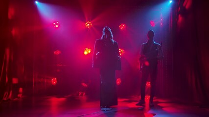 Silhouette a beautiful girl vocalist singing and gestures with his hands on stage in a vintage microphone. A brunette in a long black dress and men jacket in the rays of red spotlights. In the - Powered by Adobe