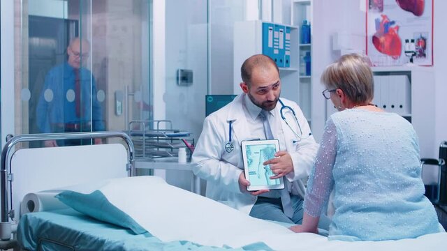 Doctor giving bones disease consultation for elderly patient, explaining osteoporosis on digital tablet PC. Health care in private clinic or modern hospital, old woman consultation senior illness
