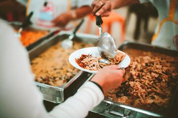 Poor people carrying plates receive food donations from volunteers : The concept of helping