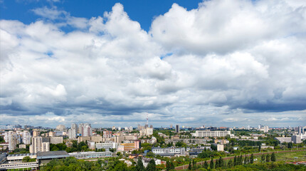 Panorama of Kyiv, with high cloudy skies over residential areas, green parks and a TV tower.