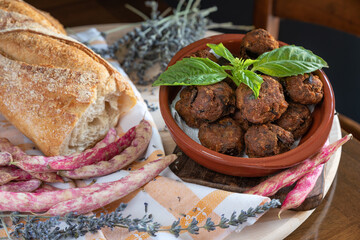 Angri, Italy. Rustic arrangement of eggplant meatballs with basil leaf, bread on wooden cutting board and cotton tea towel and lavender sprigs. Typical Italian recipe.