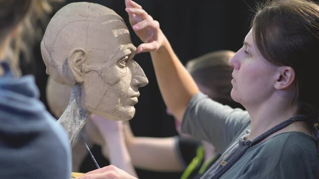 Woman sculptor at work on a sculpture of a human head. The process of restoring the shape of the eyebrows. Side view. Close up view.
