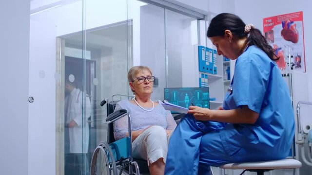 Handicapped senior woman in wheelchair talking with nurse in modern recovery clinic or hospital. Doctor help, assistance for disabled people with walking disability, medical care and treatment