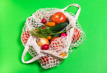 Tomatoes, cucumbers, onions, radishes and dill in a string bag on a green background