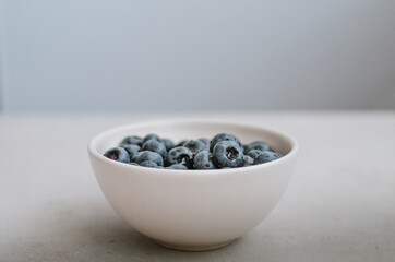 Macro of freshly picked blueberry in white bowl on blue background. Sweet ripe black berries close up in ivory plate 