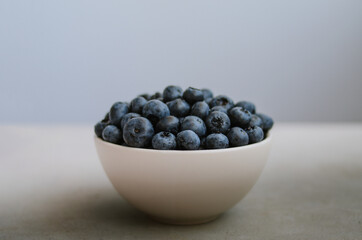 Macro of fresh ripe blueberry in ivory bowl on blue background close up. Sweet black berries isolated 