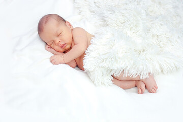 The newborn sleeps peacefully under a fluffy white blanket.