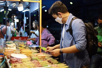 Asian man buying street food at night market.