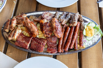 Large platter with rostille meats. National Serbian rostil in a restaurant: pork, sausages, cevapcici, rolls, french fries
