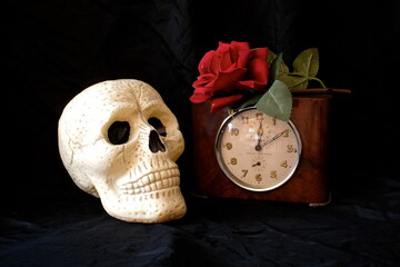 Teschio, vecchio orologio e rosa rossa su di un tavolo
