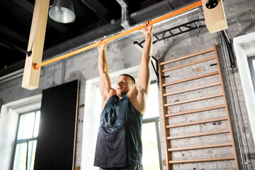 sport, fitness, exercising and people concept - man doing pull-ups on horizontal bar in gym