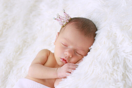Cute newborn baby girl sleeping. A newborn Princess in a crown sleeps on her arm under her head.