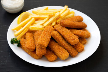 Homemade Fish Sticks and Fries with Tartar Sauce on a black surface, side view.