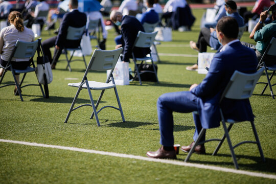 People sit on chairs apart one from another to maintain the social distance during the Covid-19 outbreak at an outdoor event on the turf of a stadium.
