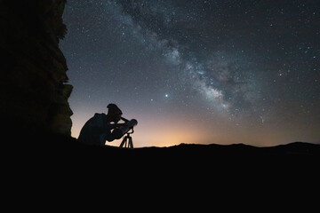 milky way in the sky and person looking through telescope