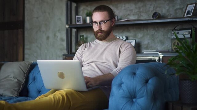 man on couch using laptop notebook looking at screen typing business message Spbd, guy hipster chatting on computer browsing. surfing internet, social media studying or working online at home