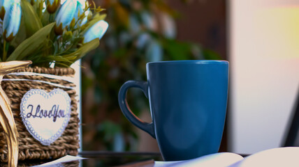 Evening coffee. Blue cup with coffee, open book and mobile phone, evening light, sunset, dusk. Atmospheric, cozy evening in the garden, green leaves, conversation. Warm light, blur bokeh.