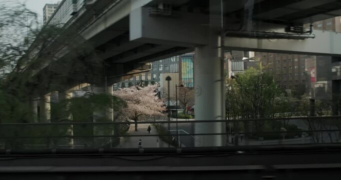 Tokyo urban industrial view with cherry blossoms from subway train window. Modern buildings and highway, bridge and river at spring.