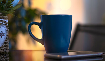 Evening coffee. Blue cup with coffee, open book and mobile phone, evening light, sunset, dusk. Atmospheric, cozy evening in the garden, green leaves, conversation. Warm light, blur bokeh.