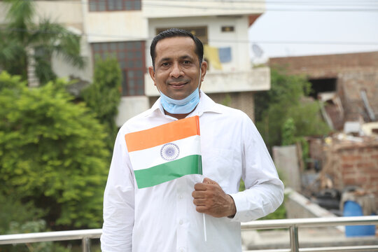 Mature man wearing mask holding waving indian tricolour flag outdoor, republic day or independence day concept during covid-19 pandemic.
