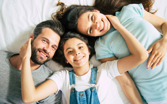 Top view photo of a beautiful happy family lying on the bed and have fun while they looking on camera