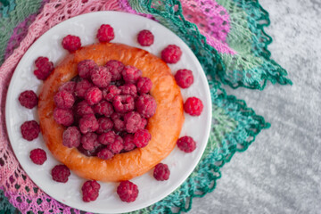 Cheesecake bun with large garden raspberries on a white plate, shot close-up