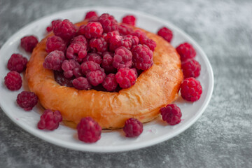 Cheesecake bun with large garden raspberries on a white plate, shot close-up