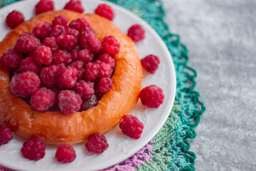 Cheesecake bun with large garden raspberries on a white plate, shot close-up