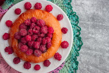 Cheesecake bun with large garden raspberries on a white plate, shot close-up