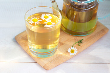 Tea from chamomile flowers in a teapot on a wooden background. Healing drink.